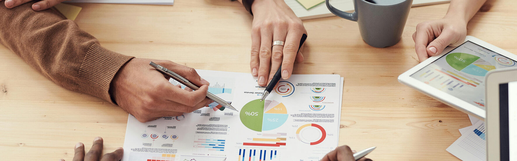 Hände von drei Personen auf einem Papier voll mit bunten Statistiken