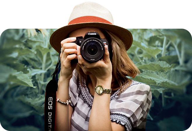 Frau hält Kamera vor Gesicht, Hintergrund Pflanzen